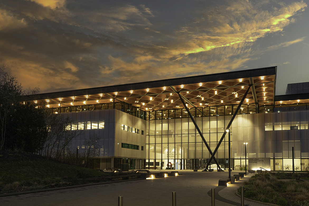 University campus at dusk, with a wide glass front and a lit timber canopy
