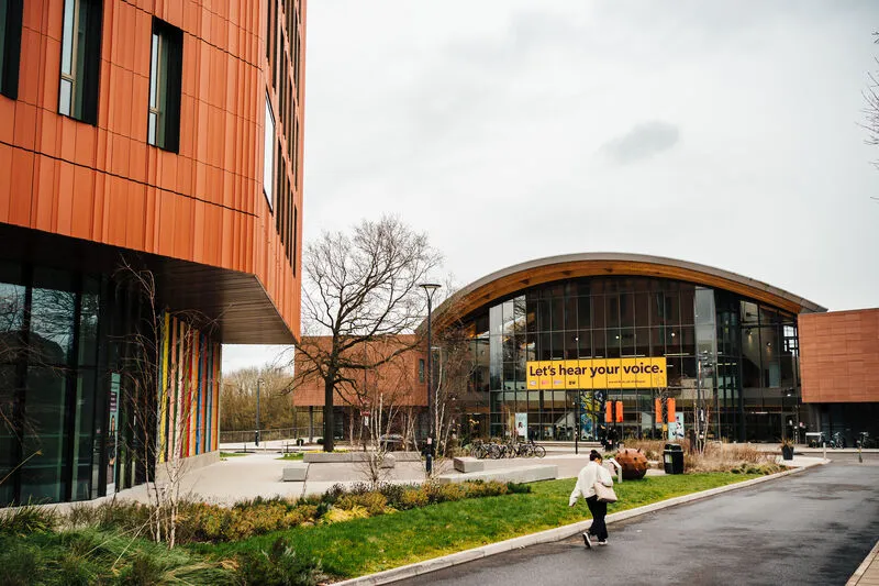 Students walking between copper-clad and glass campus buildings