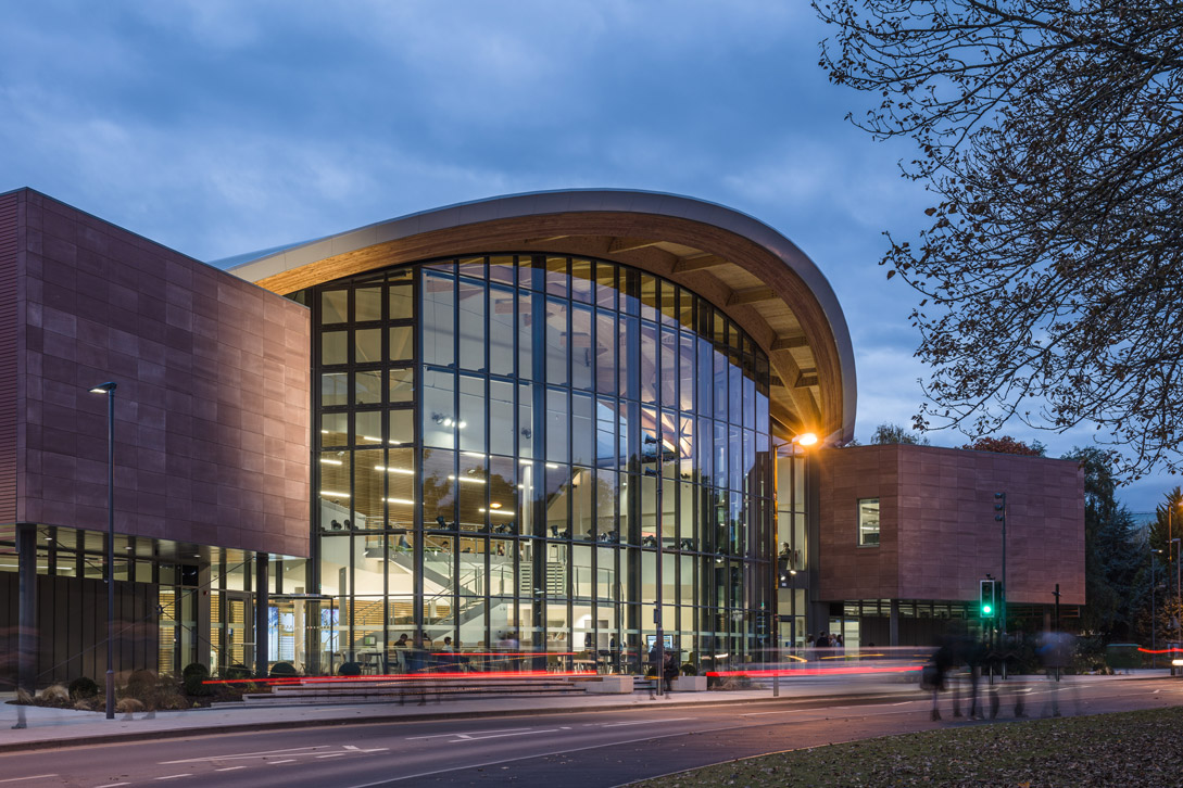 Students visible through the glass of a study building at dusk